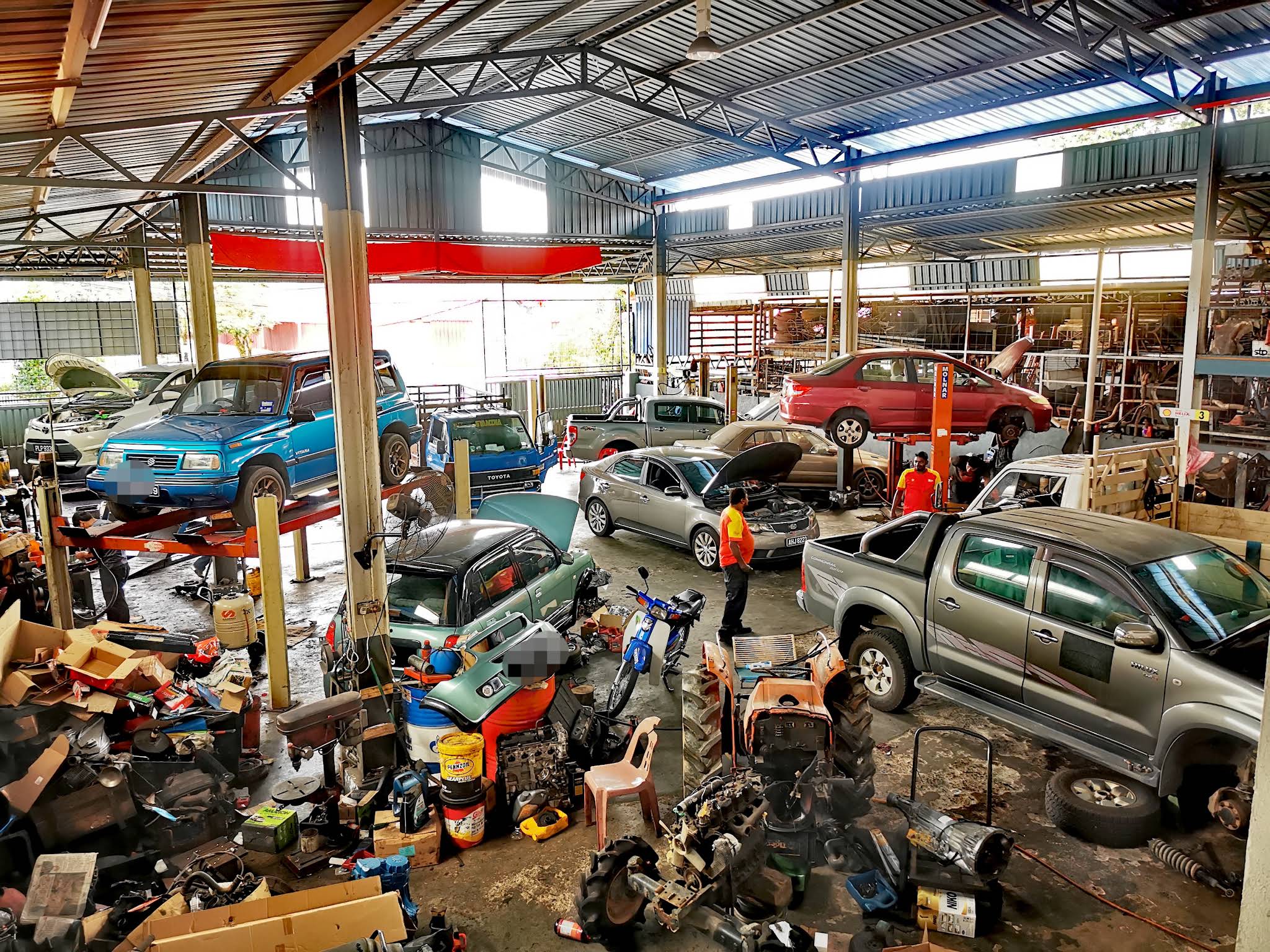 Inside the Kwong Seng Cheong Workshop garage floor, with several vehicles parked and up on lifts for repair.